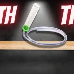 youtu be thumbnail with a black background and a wooden table taking up most of the frame. A gravel vacuum is on top of the table with a spotlight pointed down onto it. "With This" is written in big white letters across the top